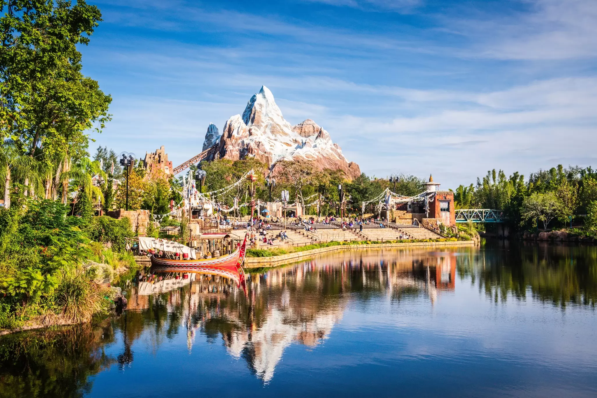 A large artificial snow-capped mountain beside a lake surrounded by a metal roller coaster, at Walt Disney World®, Orlando
