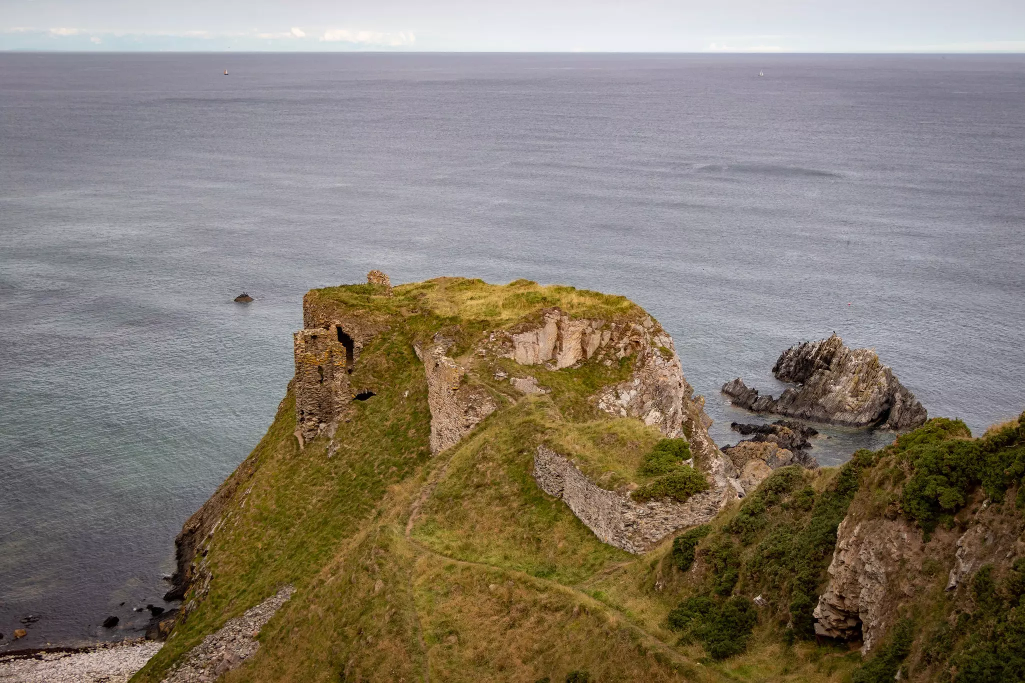 A wide view of a ruined castle on a bluff overlooking the sea