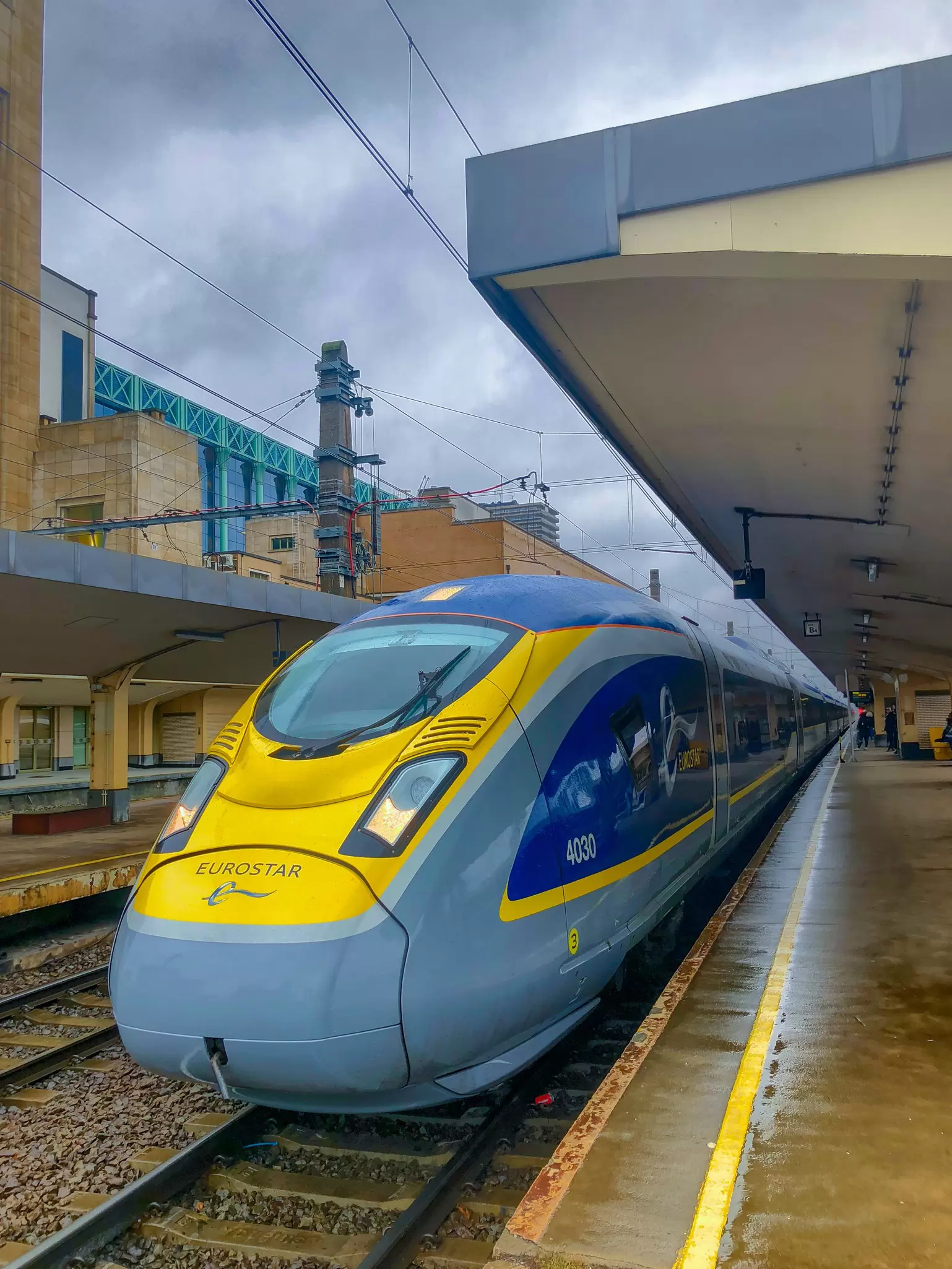 Blue and yellow Eurostar high-speed train waiting at a covered station platform on a grey day