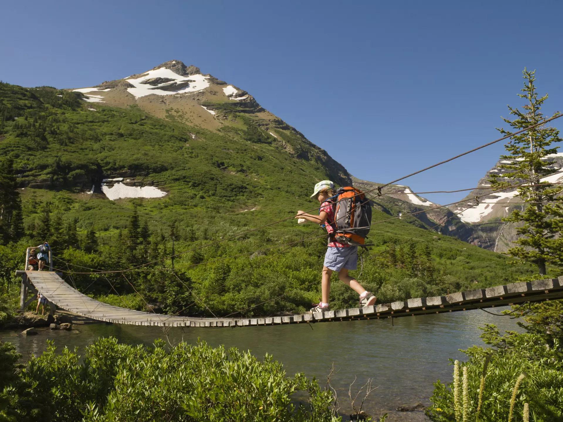 A young girl hikes over a suspension bridge in Glacier National Park, Montana.
