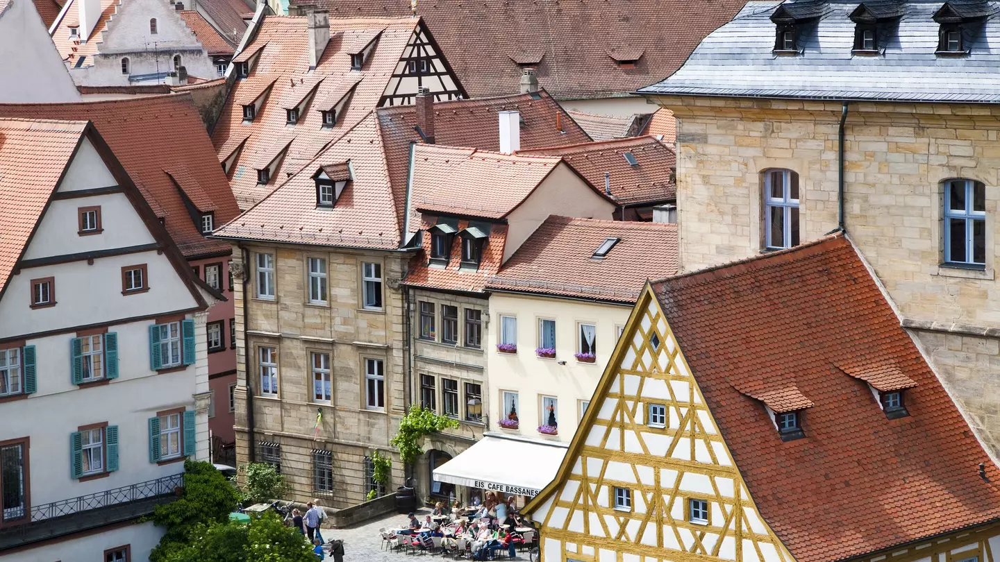 Red-tiled rooftops lead down to a city square where people are having a drink outside a cafe