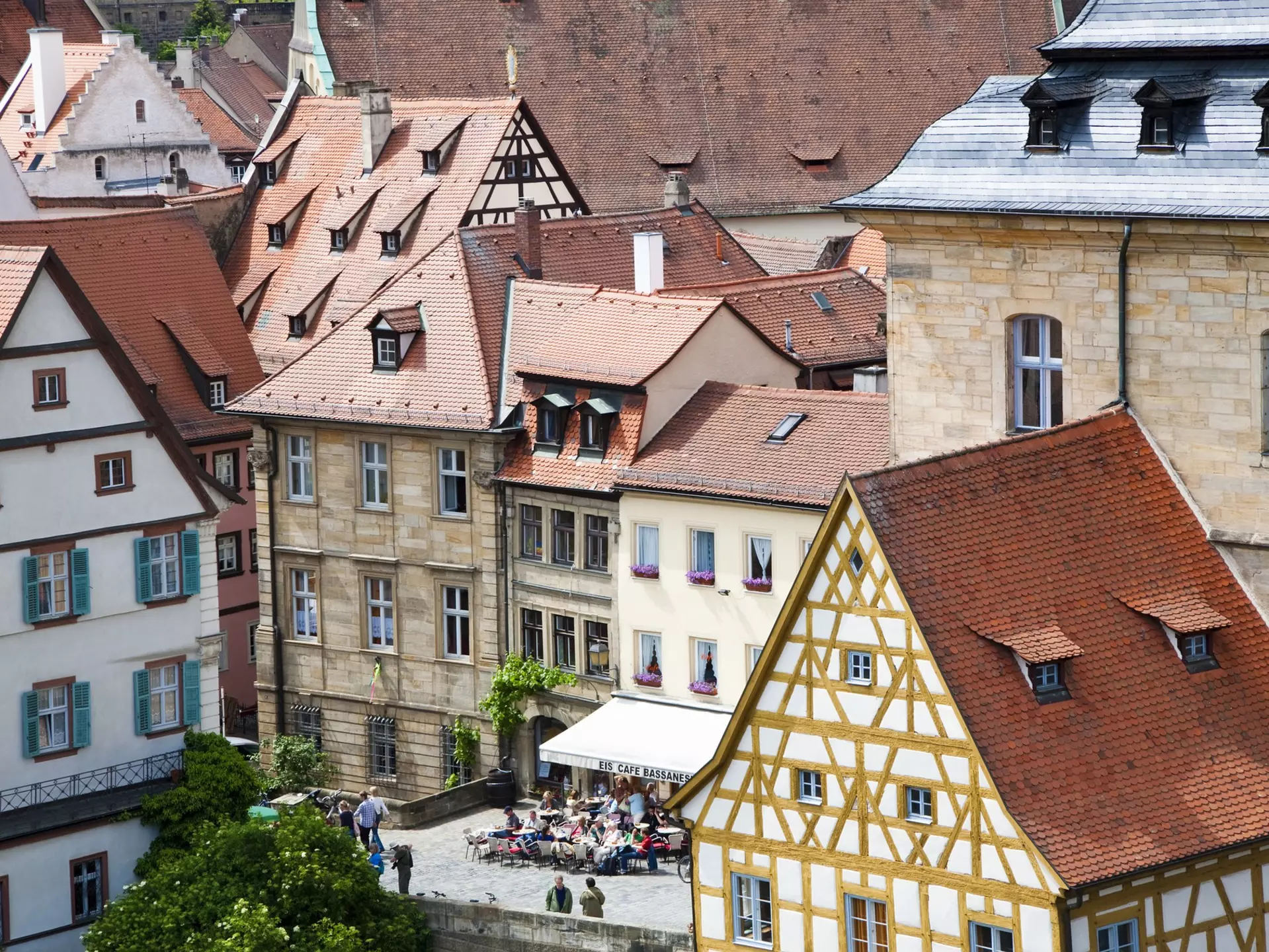 Red-tiled rooftops lead down to a city square where people are having a drink outside a cafe