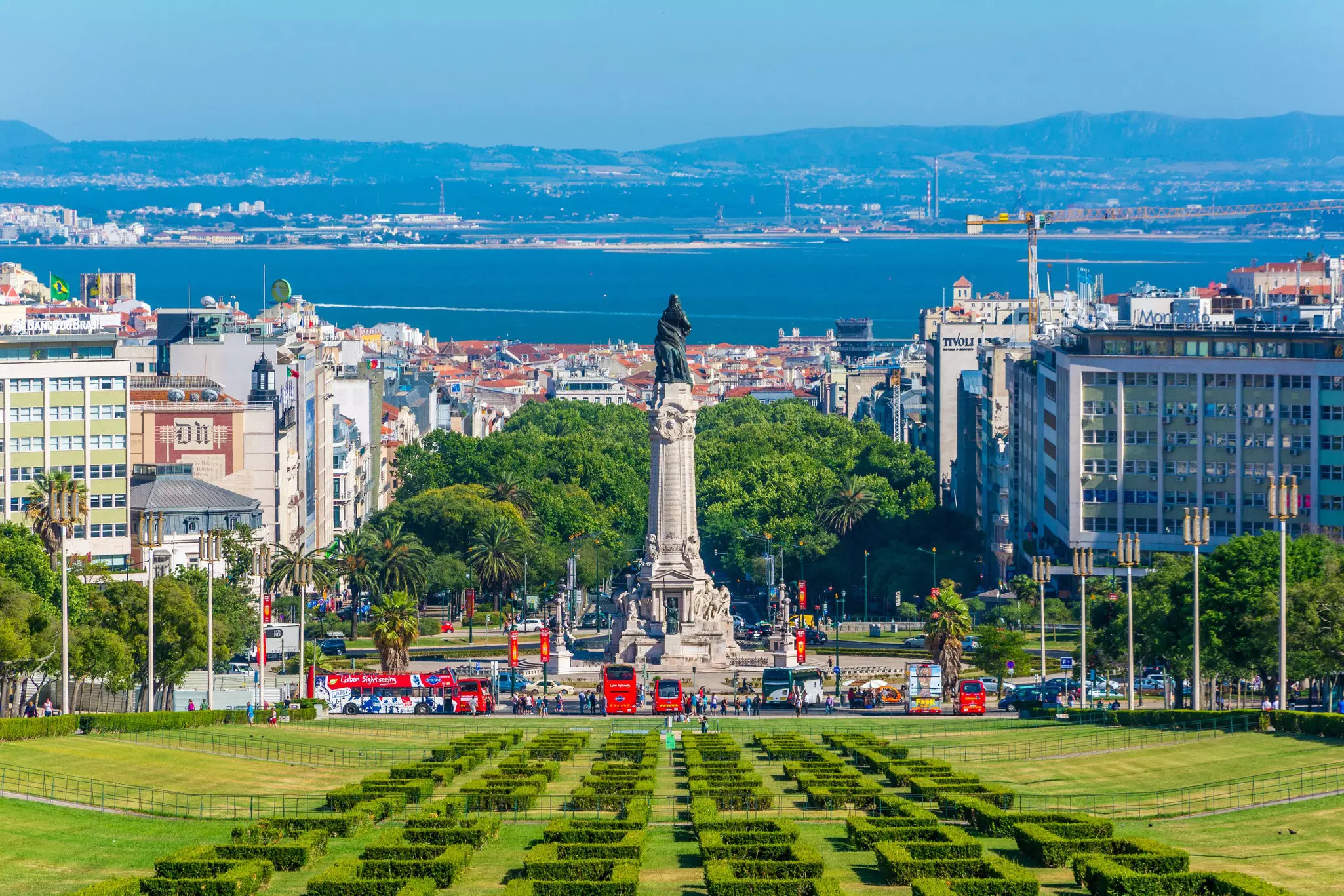 Lush manicured gardens in front of a tall column with a bronze statue of a man on it with a vast view out to a river.