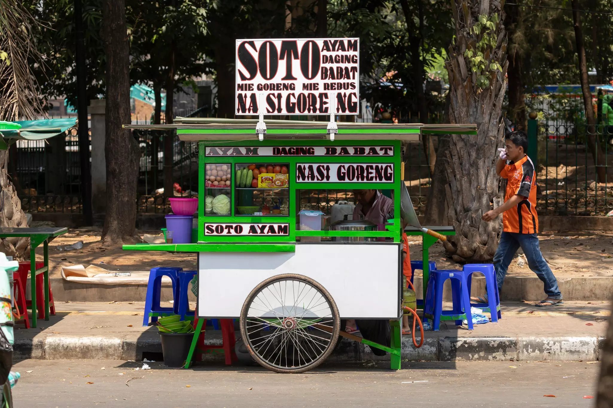 Small green and white street food stall with pedestrian walking past on a sunny day.