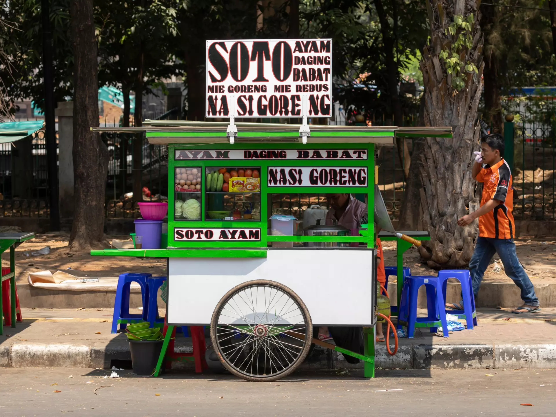 Small green and white street food stall with pedestrian walking past on a sunny day.