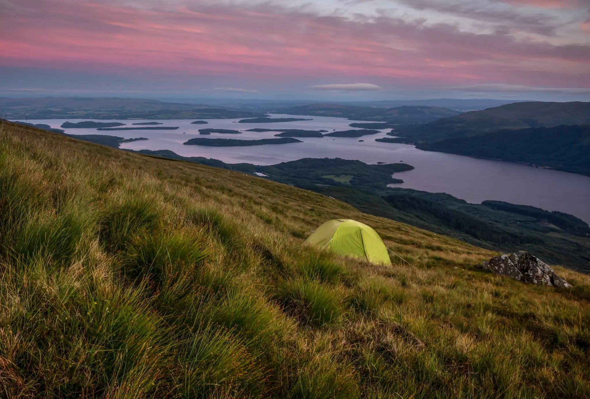 Green tent on Ben Lomond at dusk with pink clouds, on the slope of the hill overlooking Loch Lomond, Loch Lomond & The Trossachs National Park, Scotland.