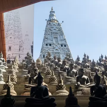 Low angle view across dense rows of stone meditating Buddhas on the open air terrace pointing toward the shining silver stupa of the Gangaramaya Temple in Colombo, Sri Lanka.