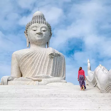 A teenager climbs steps upwards towards a vast white marble Buddha statue
