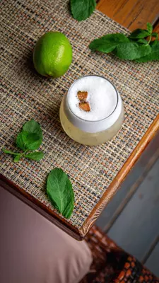 An overhead view of a pale yellow drink in a clear glass with a foamy white top.