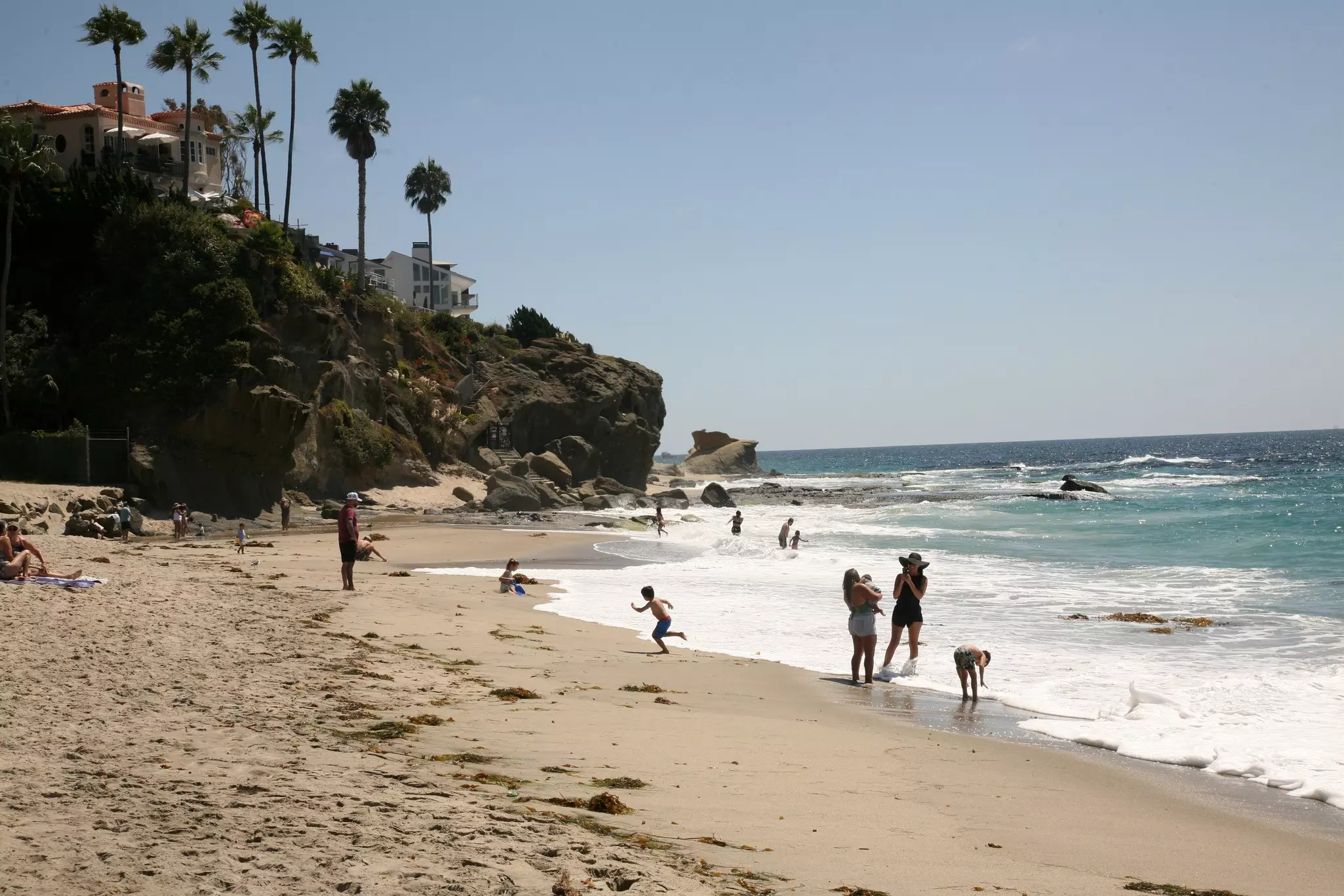 Children play and people stand at the water's edge on a sandy ocean beach in California.