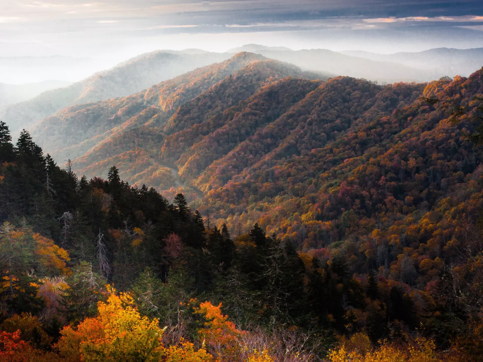 A view of the sun rising between mountains in the Smoky Mountains, USA. The mountains are covered in thick forest.