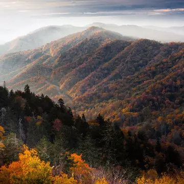 A view of the sun rising between mountains in the Smoky Mountains, USA. The mountains are covered in thick forest.