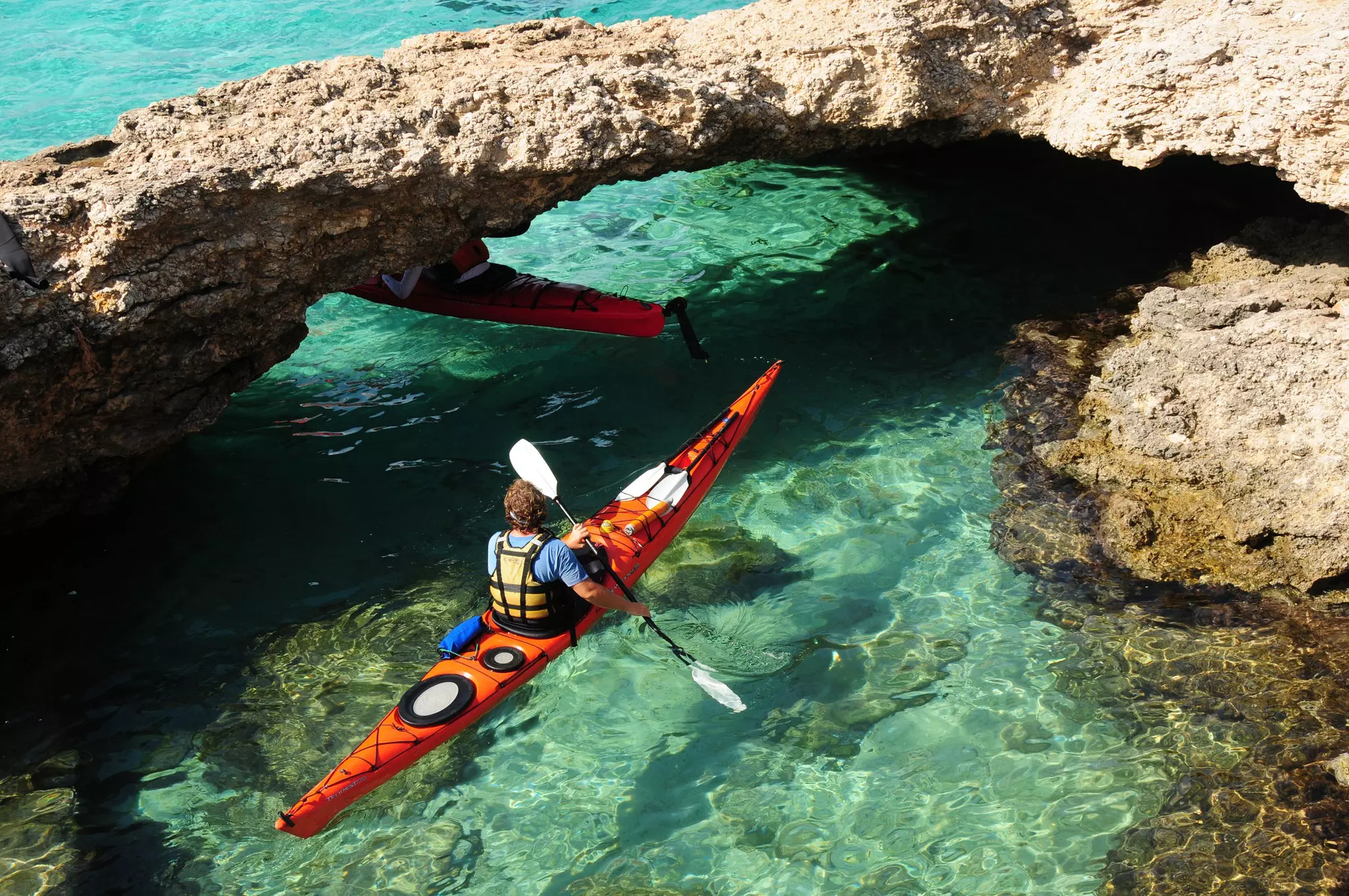 A kayaker paddling under a natural limestone arch in the Blue Lagoon, Comino.