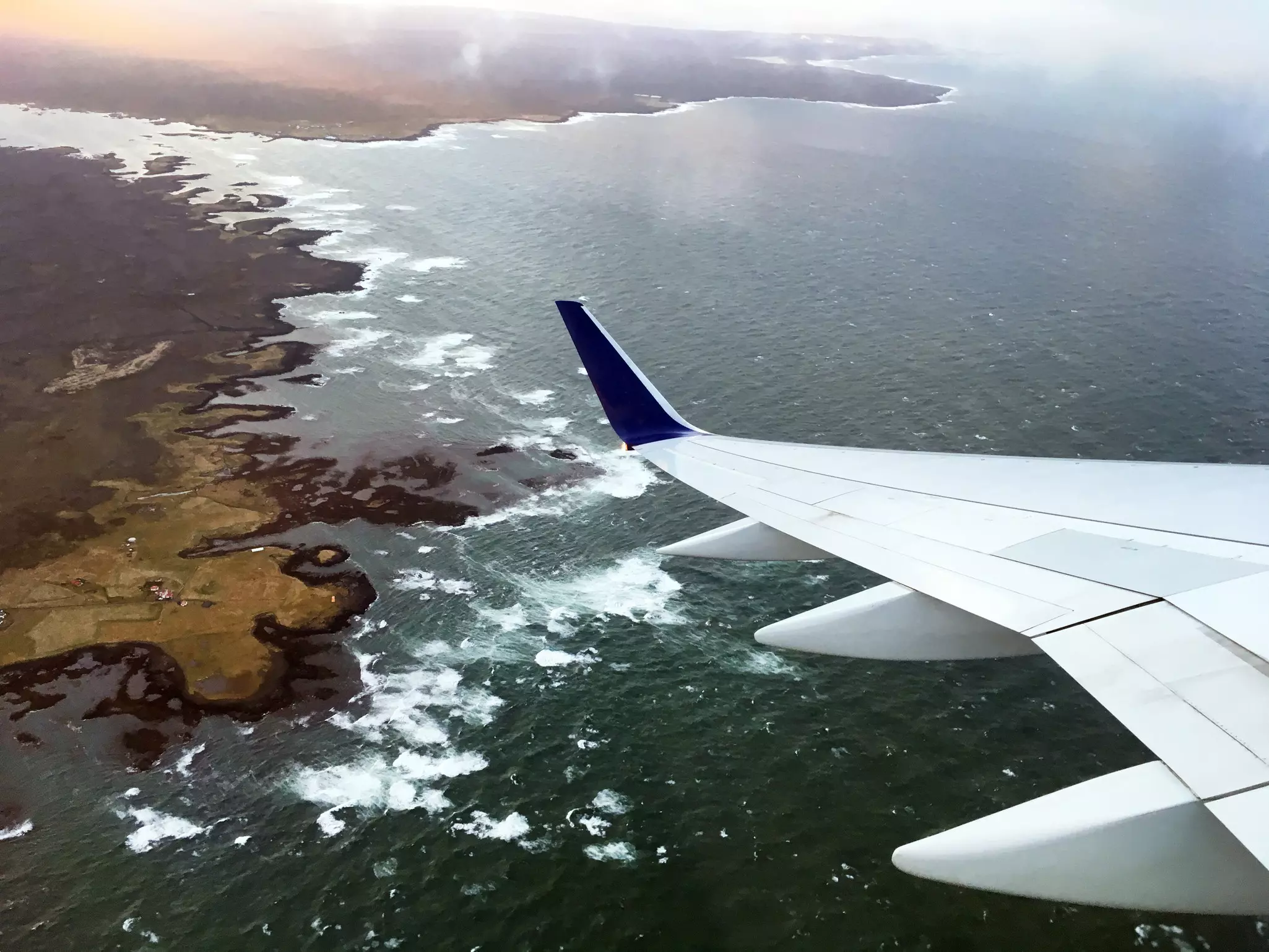 An aerial view of the coast of Iceland with a plane wing in the foreground.