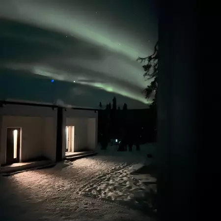 Streaks of northern lights over a squat square building in the snow in Alaska.