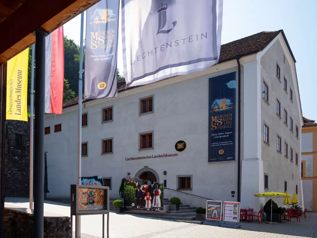 White museum building in Vaduz with tall exhibition banners hanging beside its entrance under a blue sky