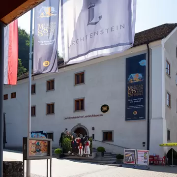 White museum building in Vaduz with tall exhibition banners hanging beside its entrance under a blue sky