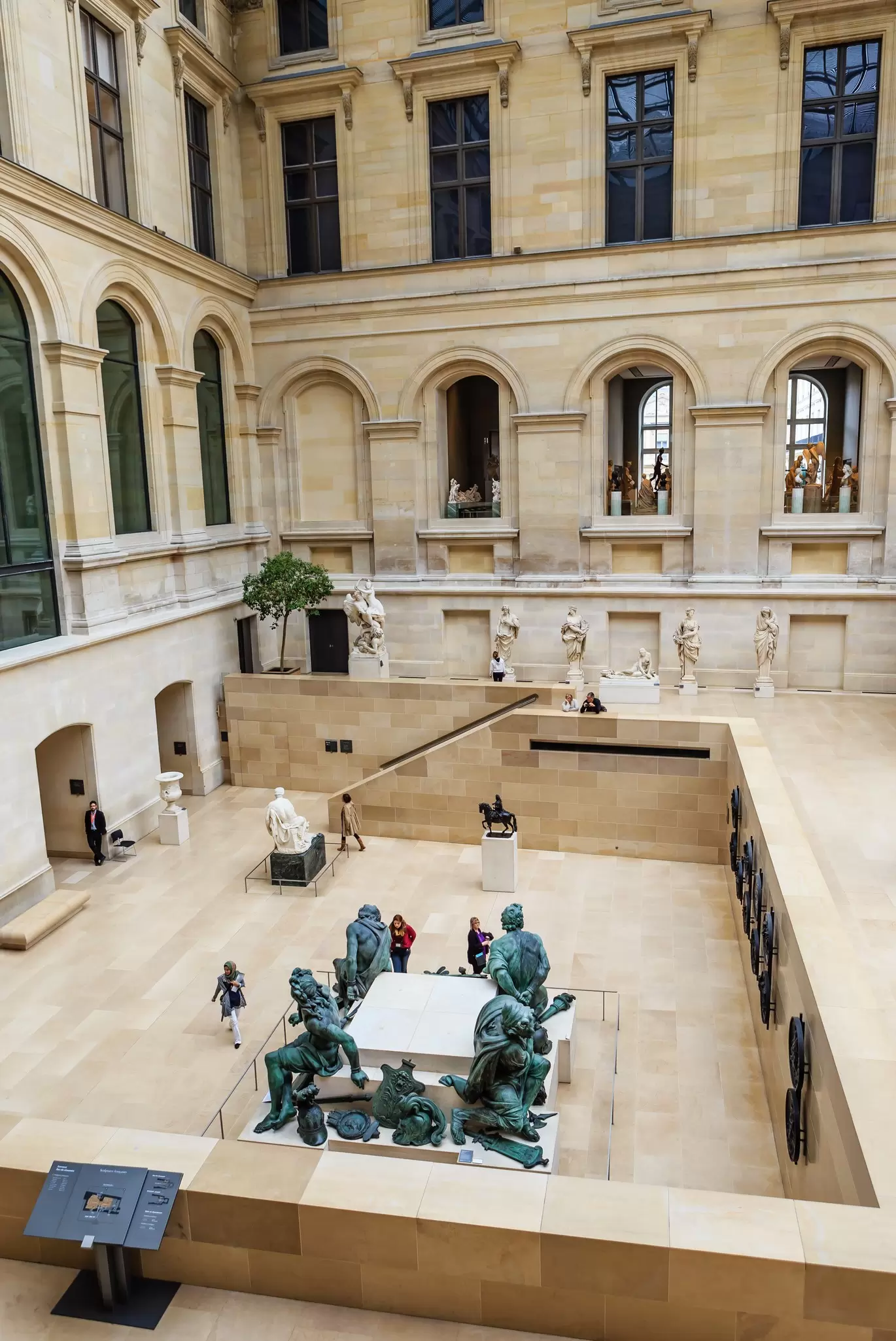 Visitors examine the sculptures in the Puget courtyard, inside the Louvre Museum, Paris, France.