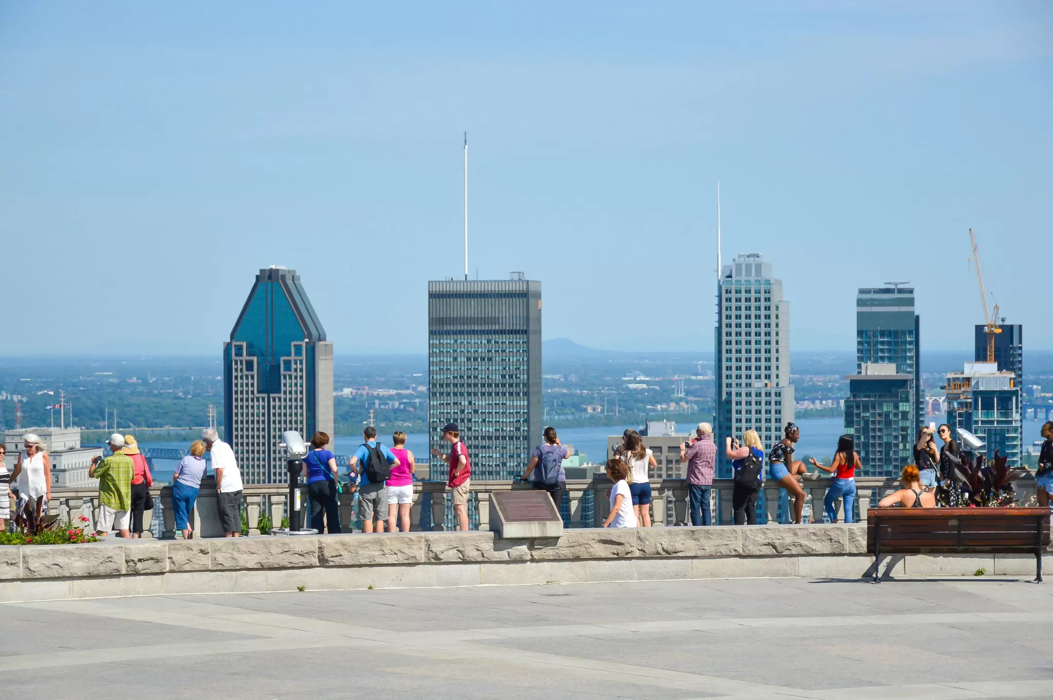 A row of people stand at a viewpoint looking towards a city skyline
