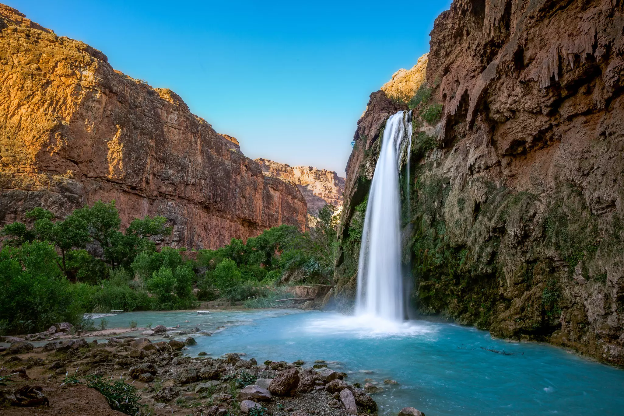 A waterfall into a turqoise pool surrounded by red rocks