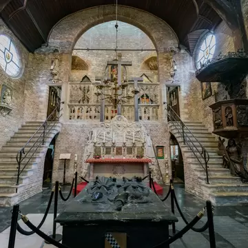 Jeruzalemkerk interior in Bruges: brick walls, two staircases to a raised crucifix gallery, and a black tomb with effigies