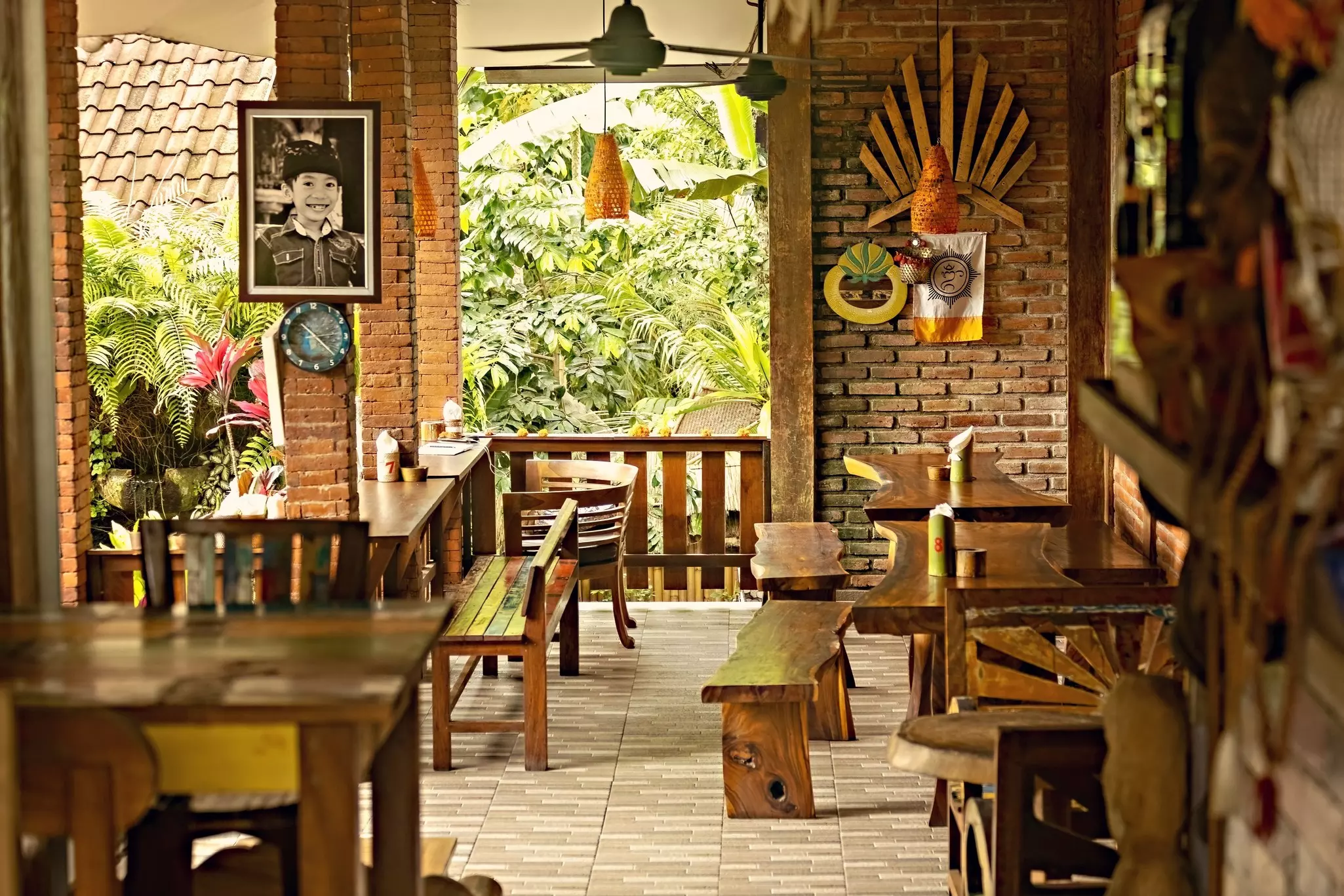 Tables and chairs are pictured in a cafe with windows open to a verdant area outside.
