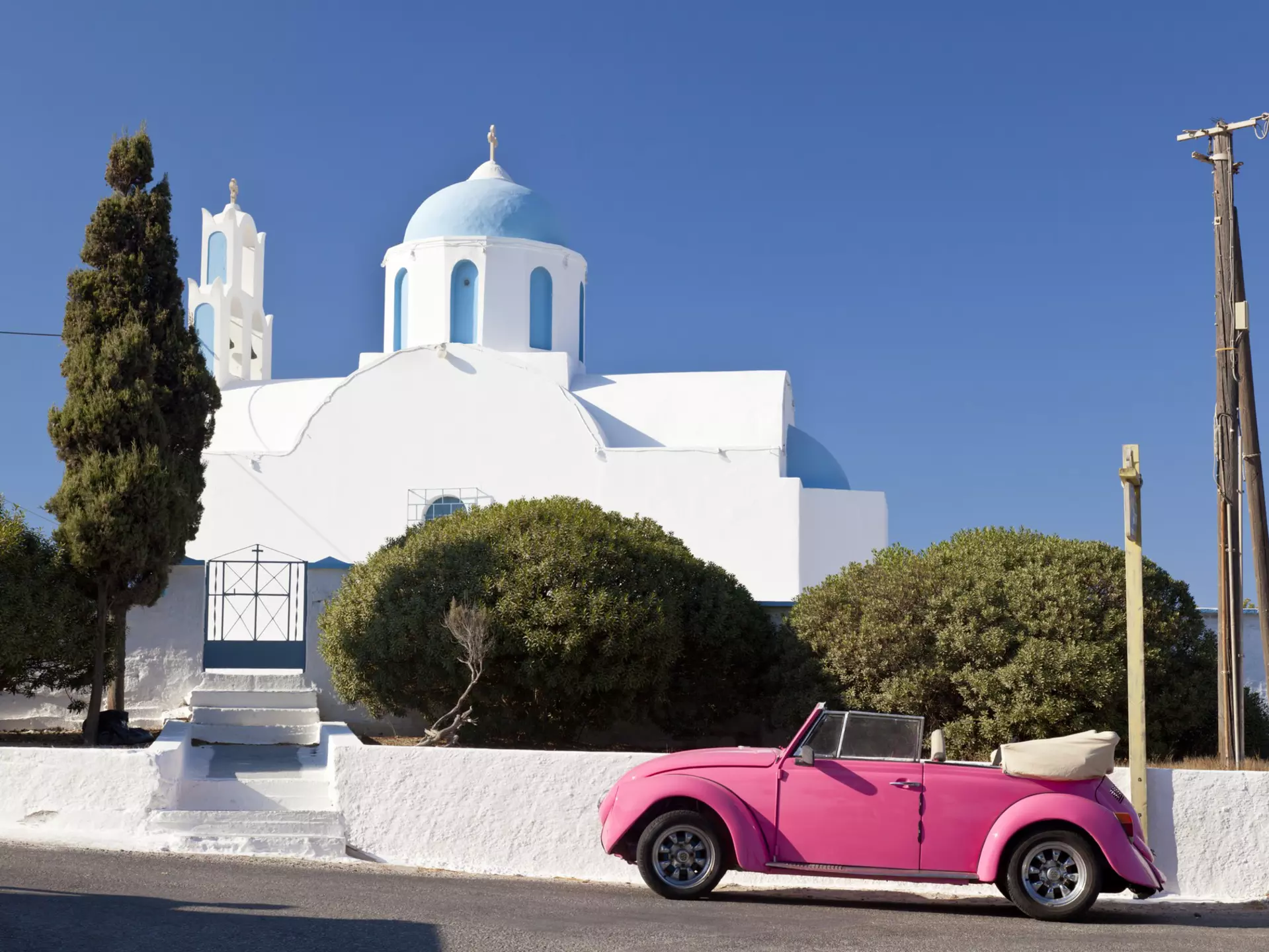 A pink Volkswagen Beetle in front of a chapel on Santorini, Greece