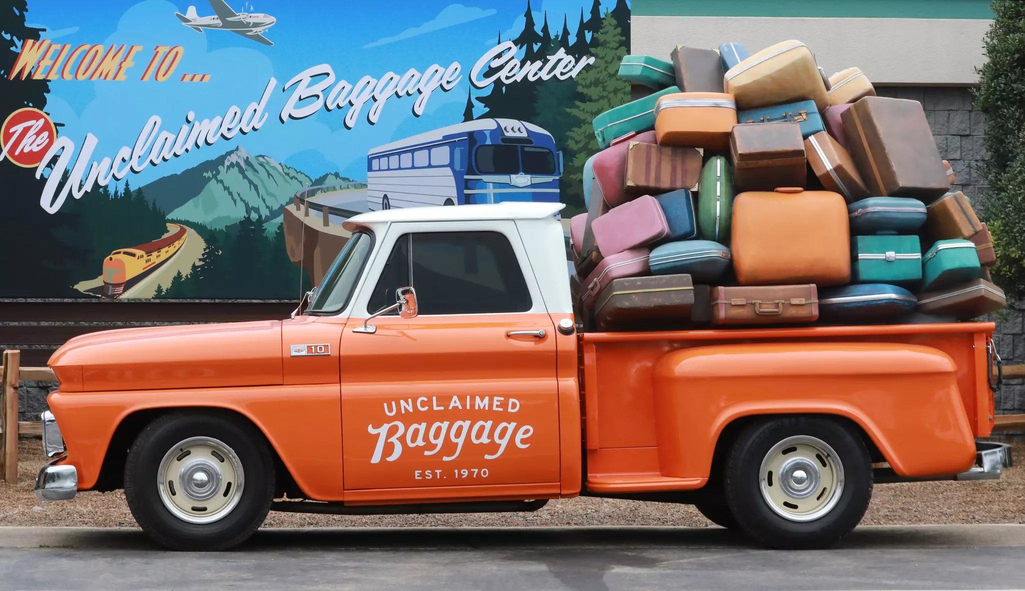 An orange pickup truck filled with suitcases, labeled "Unclaimed Baggage"