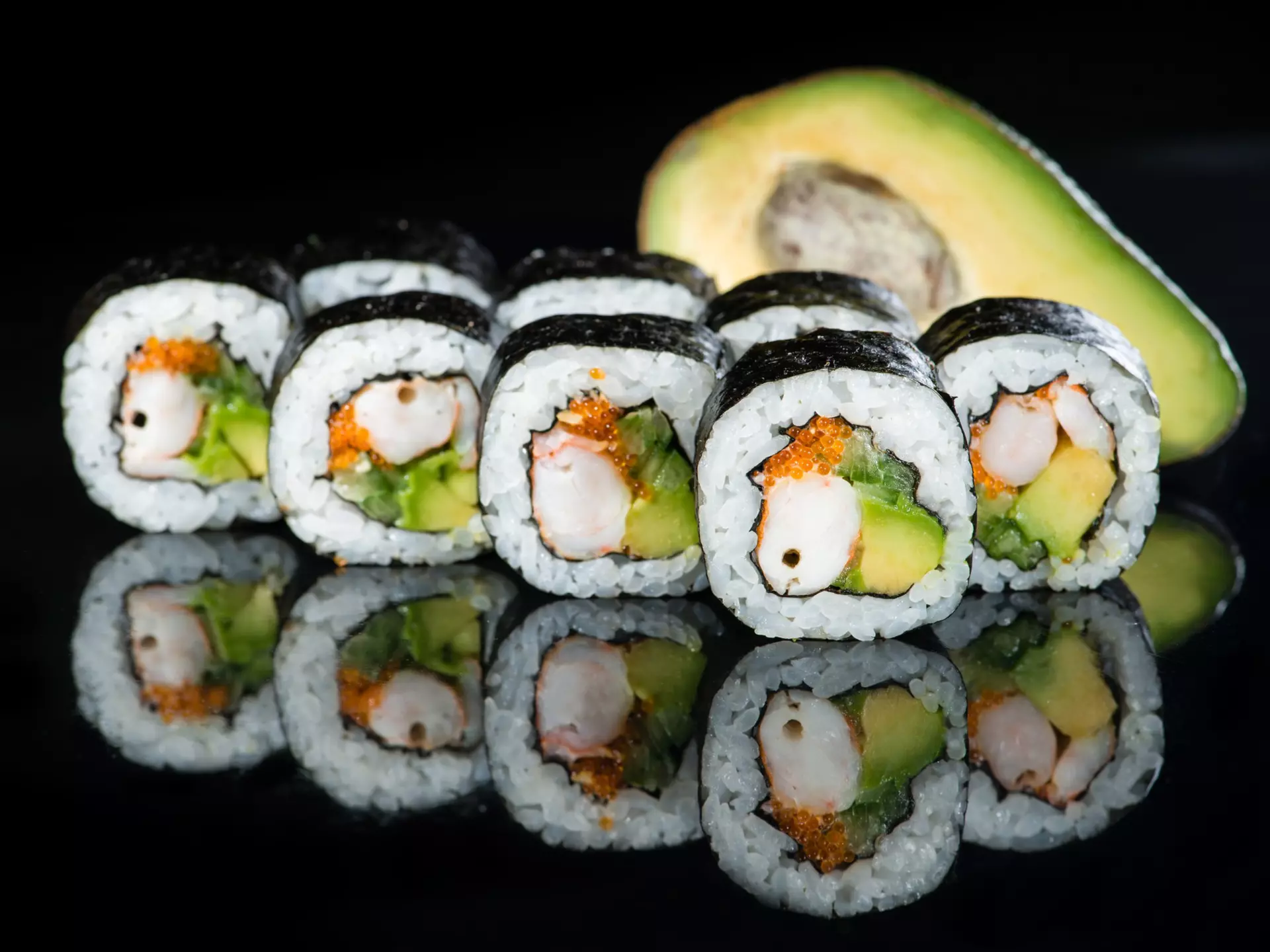 Fresh delicious Japanese sushi with avocado, cucumber, shrimp and caviar on dark background; California roll