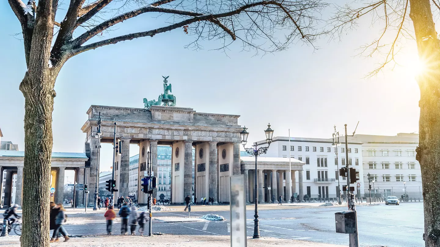 Out-of-focus people walk along a winter city street with a large stone gate along the roadway on a sunny day.