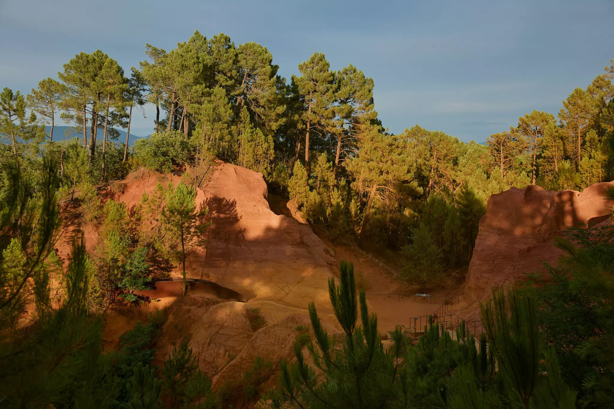 An orange and red sandy landscape with sheer cliffs covered in woodland.