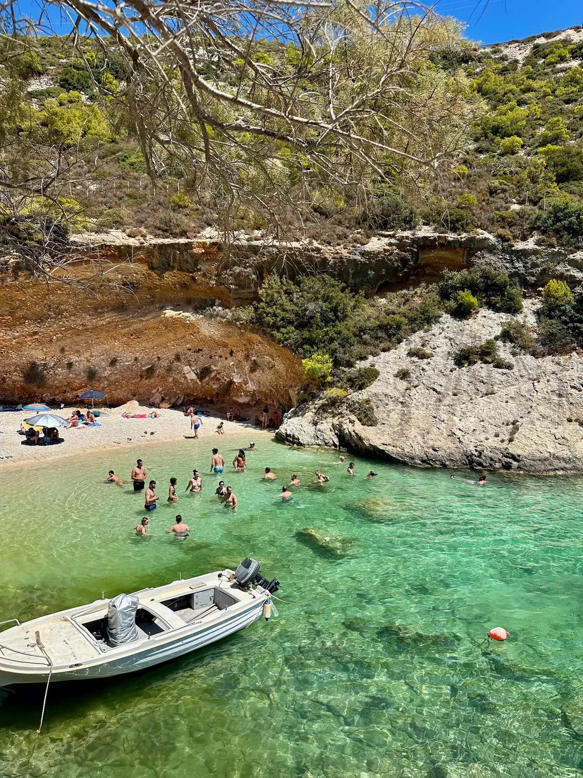 A boat docked in a small bay while people swim in clear waters around it