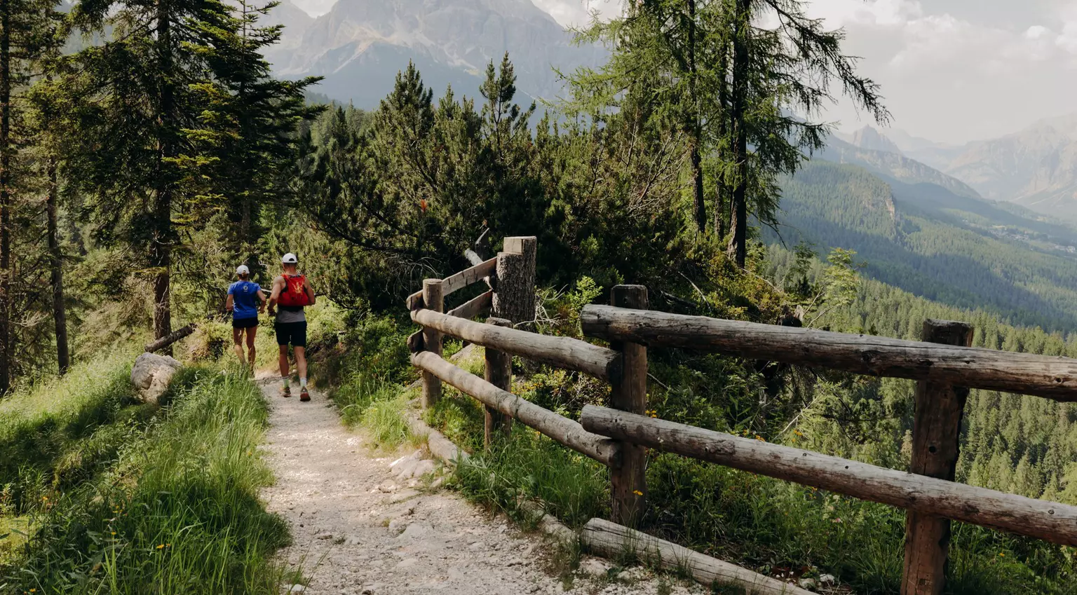 Hikers on a dirt trail lined with a wooden fence