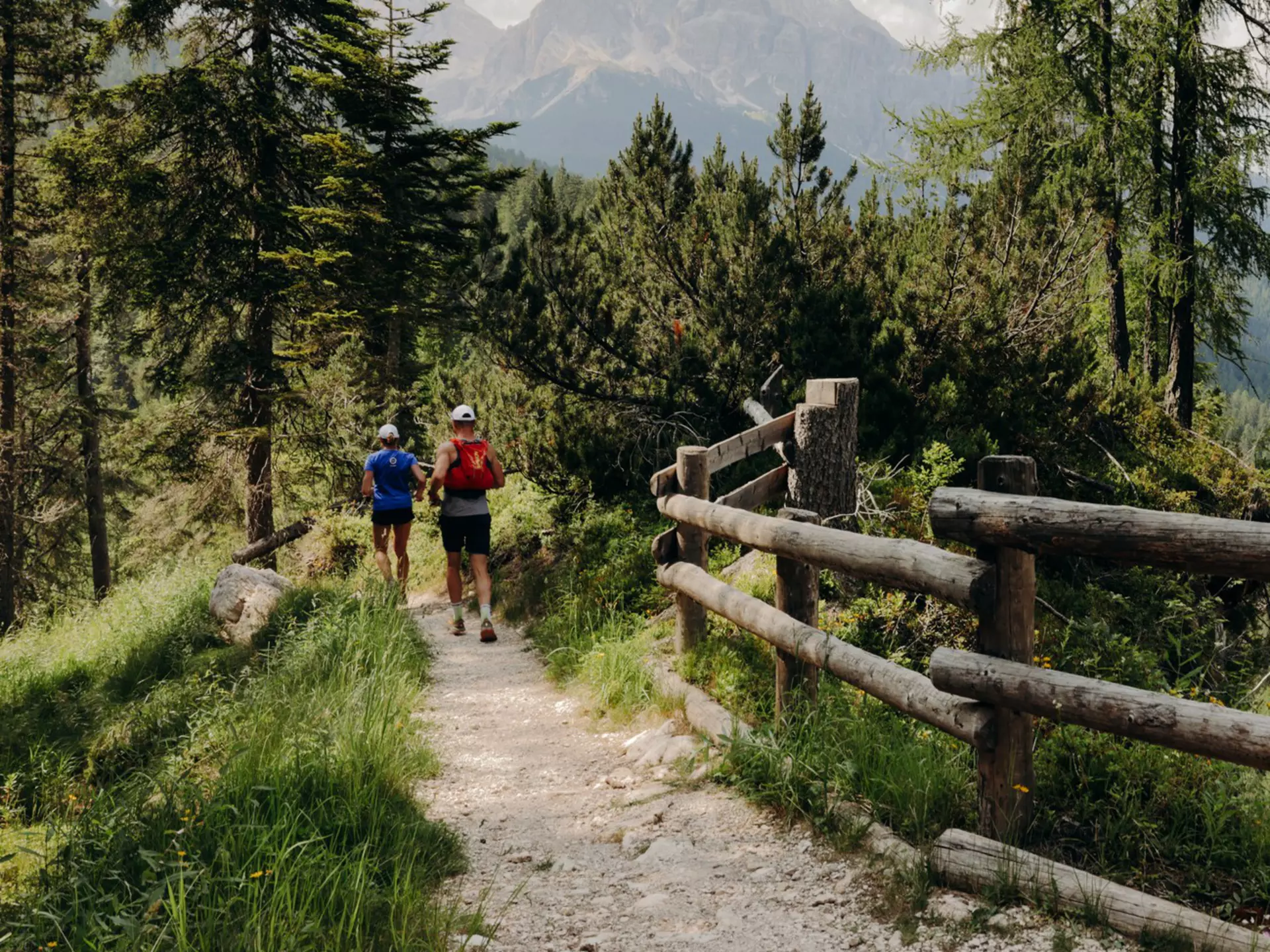 Hikers on a dirt trail lined with a wooden fence