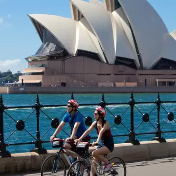 Two bikers biking past the Sydney Opera House as part of Bonza Bike Tours in Sydney, Australia.