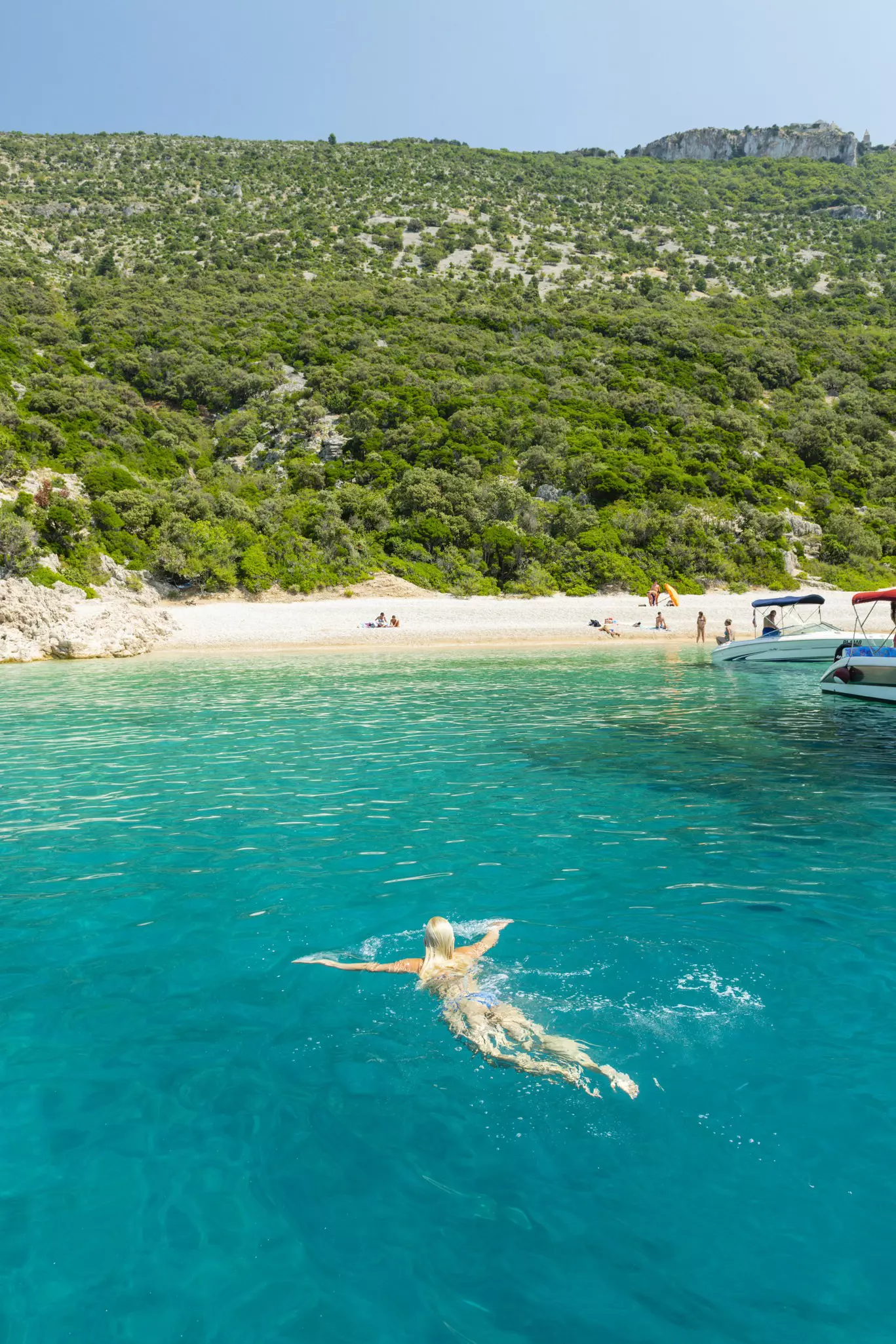 A woman swims through turquoise water near a beach backed by dense undergrowth