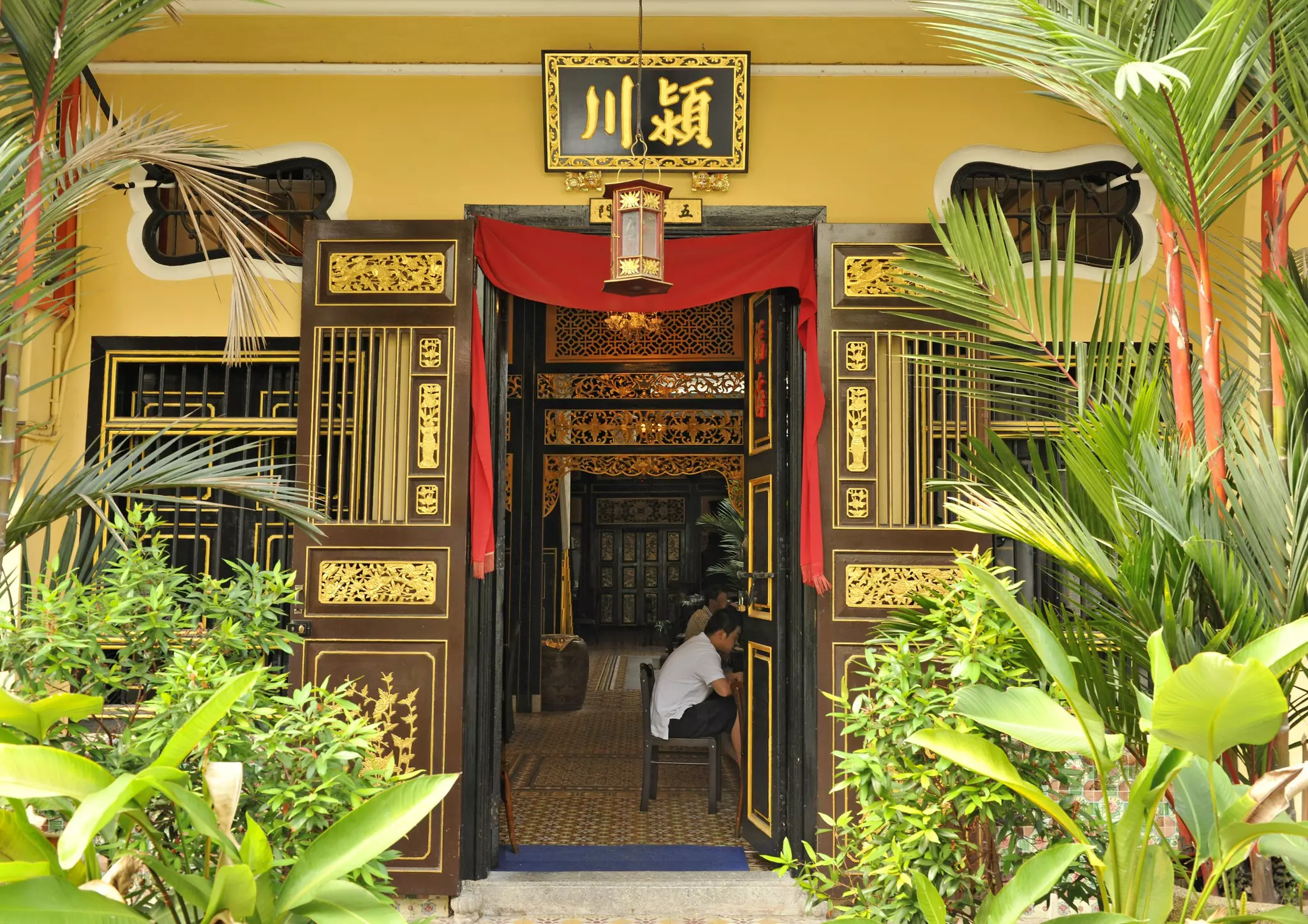 A doorway surrounded by ornate detail in gold leads to a small shop in Malaysia.