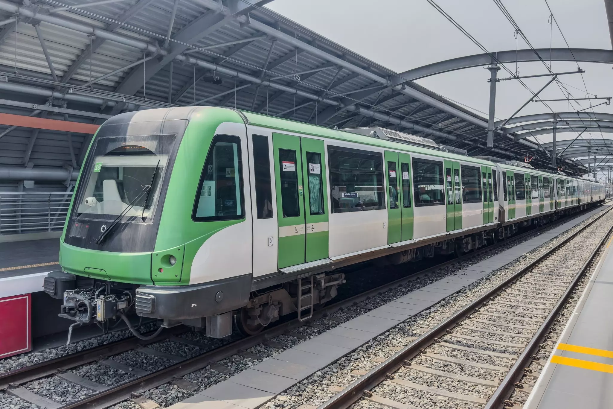 A light rail train with cars painted green pulls into a station in a city.