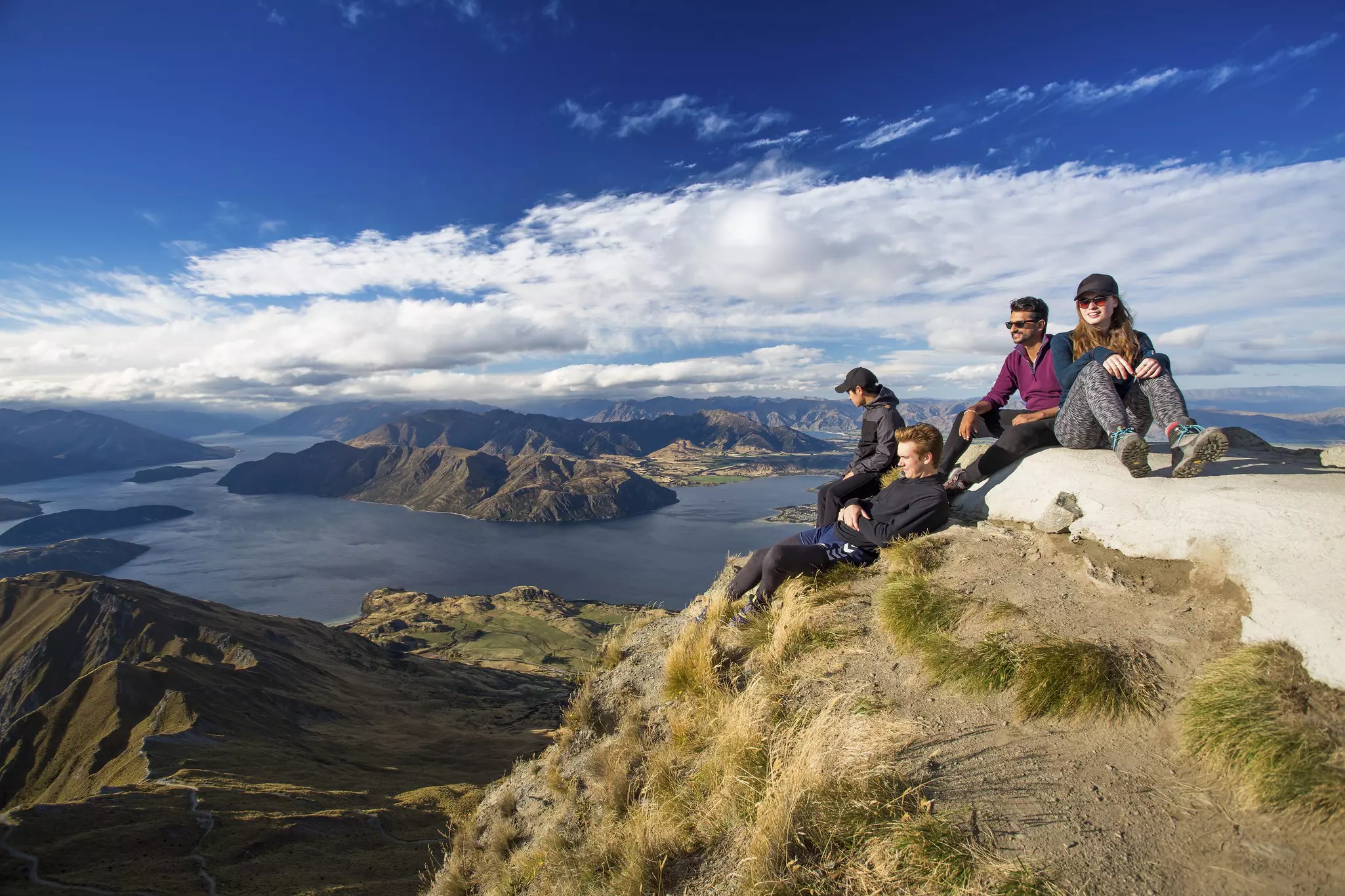 A group of four hikers rests after the strenuous hike to the top of Roy’s Peak, which has gorgeous views of Lake Wanaka below