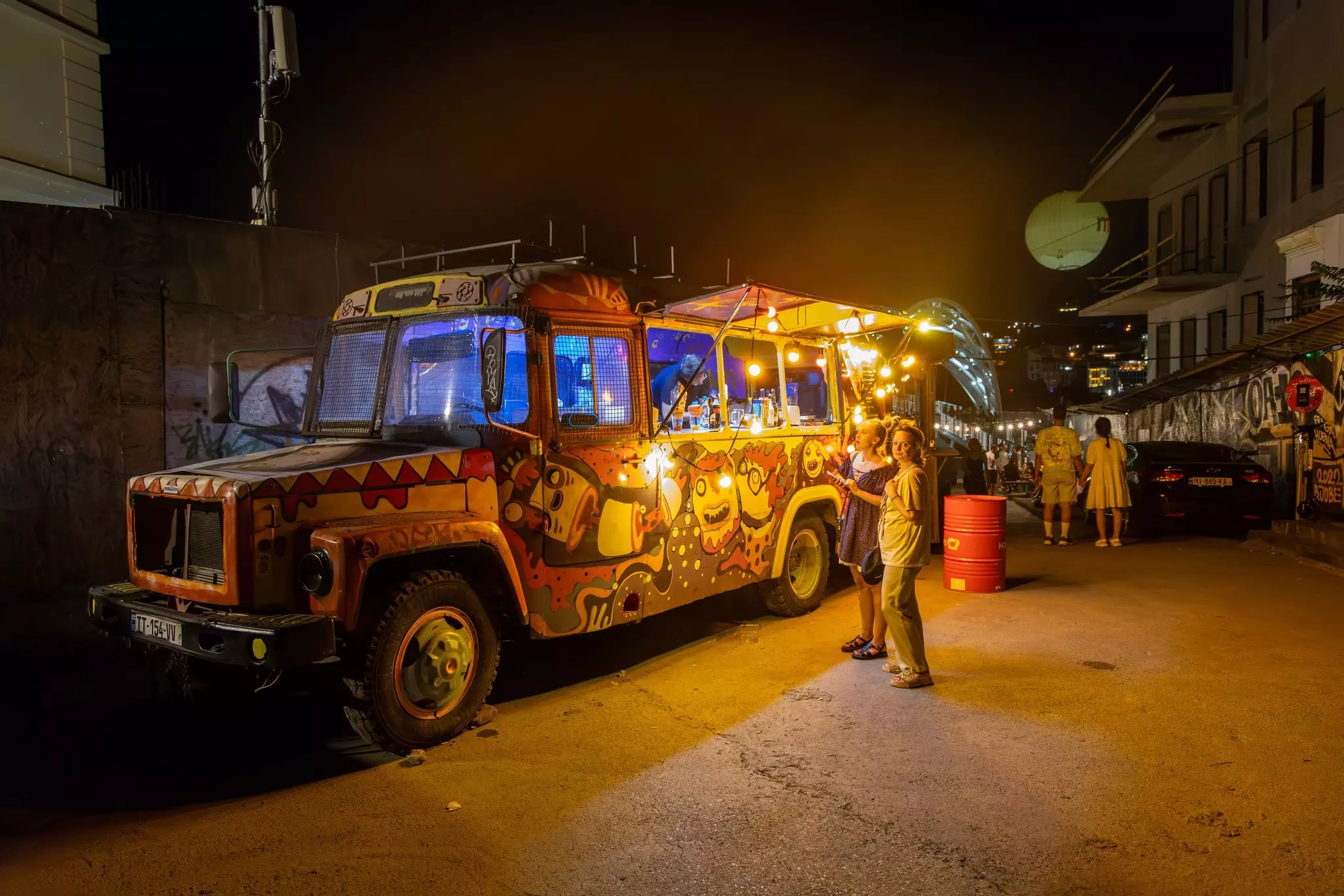 People stand in front of a painted food truck in a city at night.