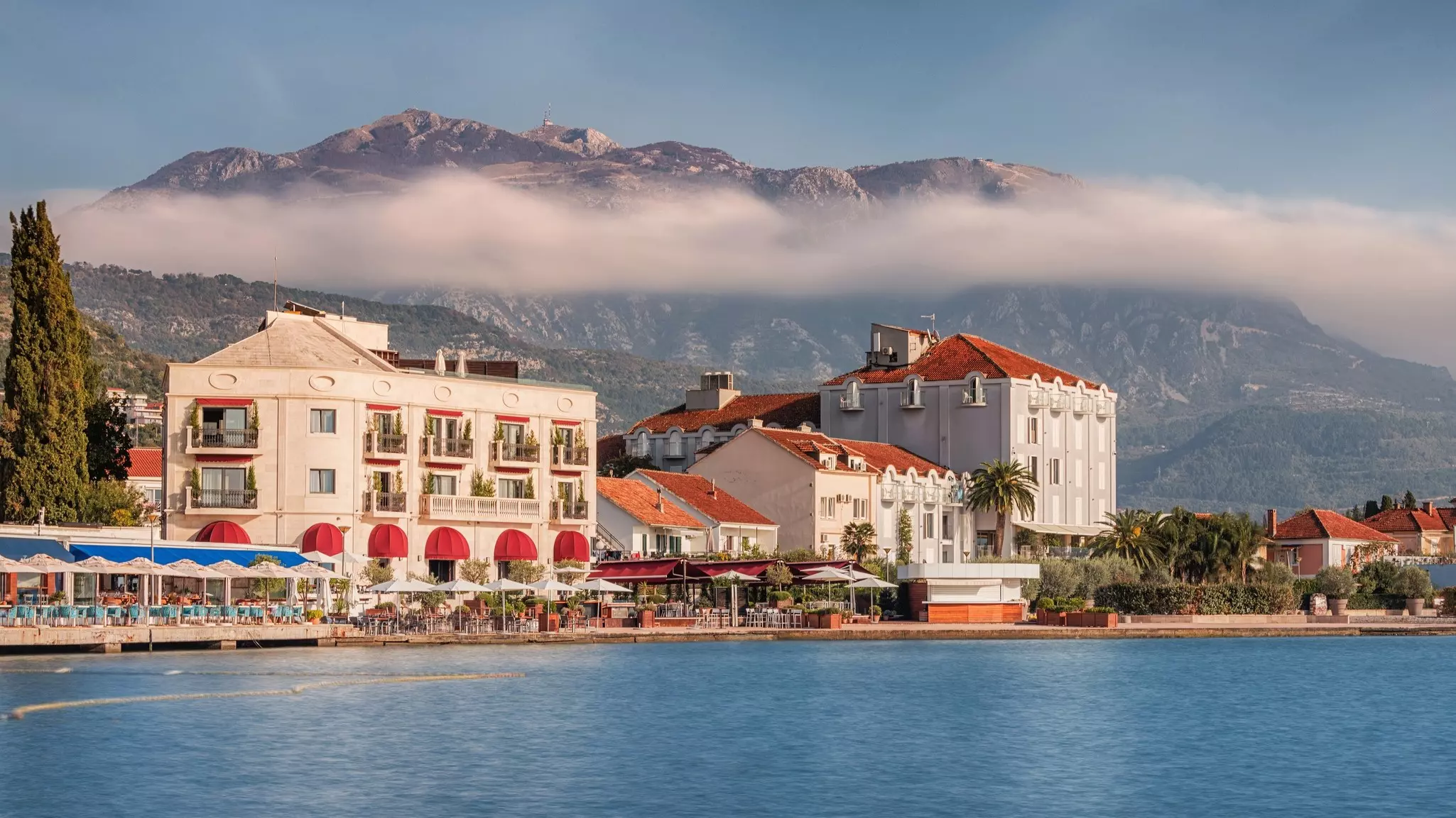 Harborside restaurants and hotels in a small town. Cloud covers the mountains behind.