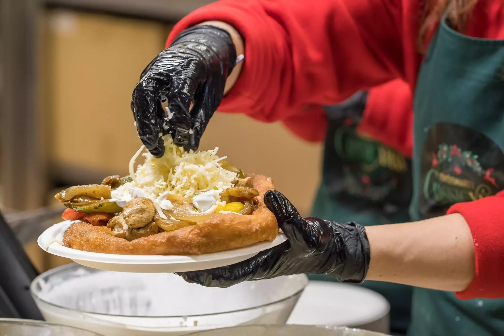 A vendor putting toppings on a piece of fried dough on a plate.