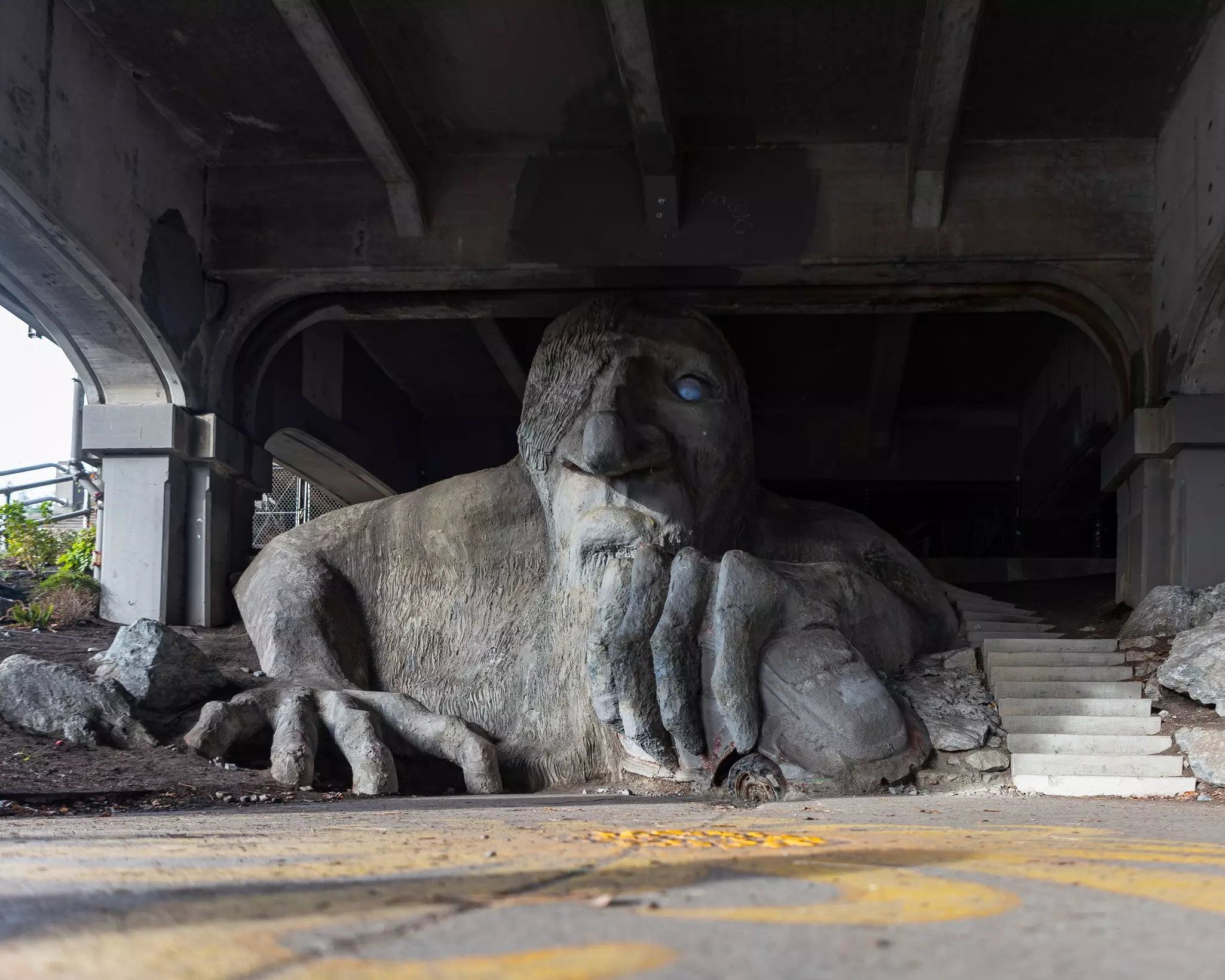 A large sculpture under a bridge of a troll under eating a car