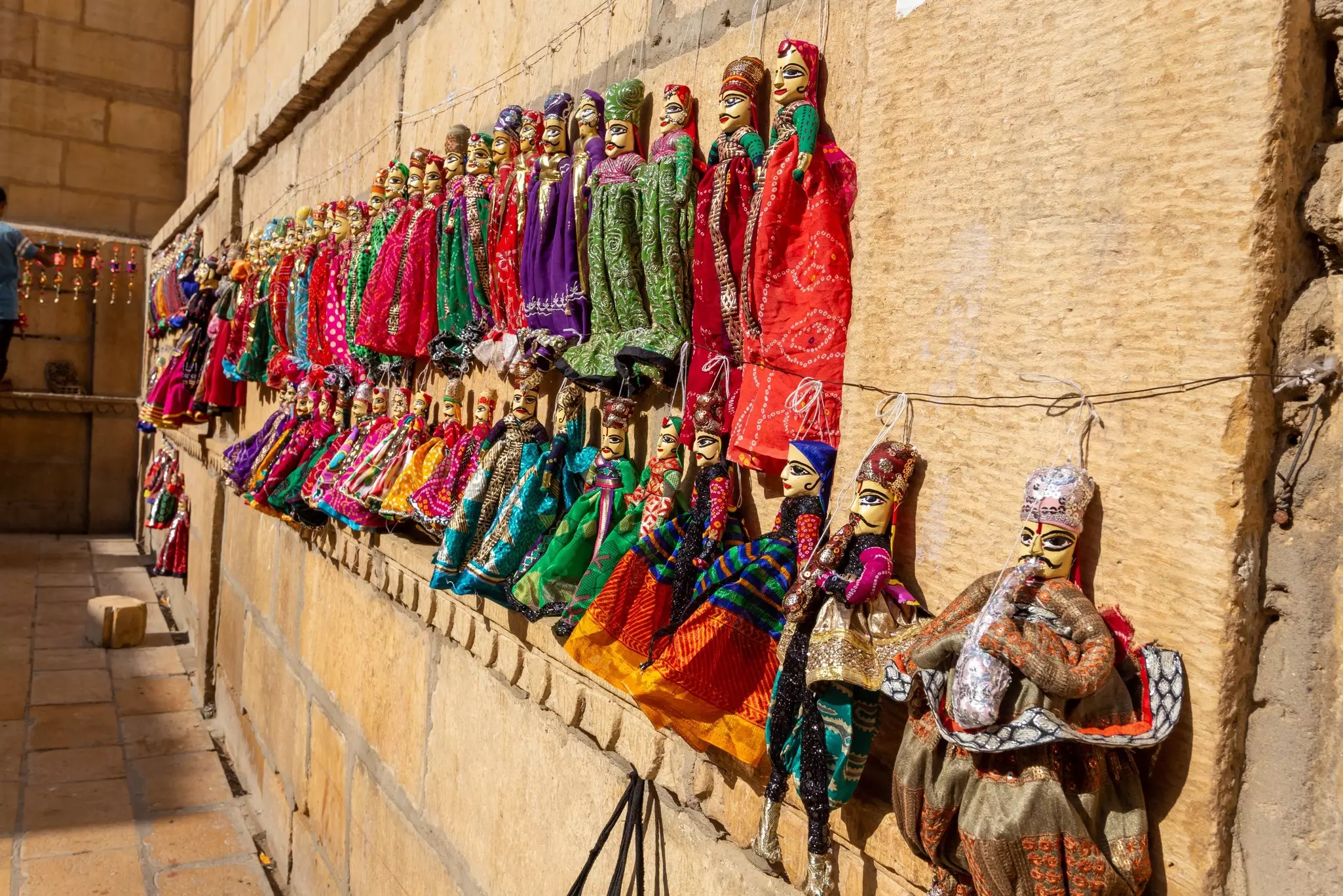 An assortment of traditional puppets in brightly colored costumes is on display, pinned to strings on a sandstone wall