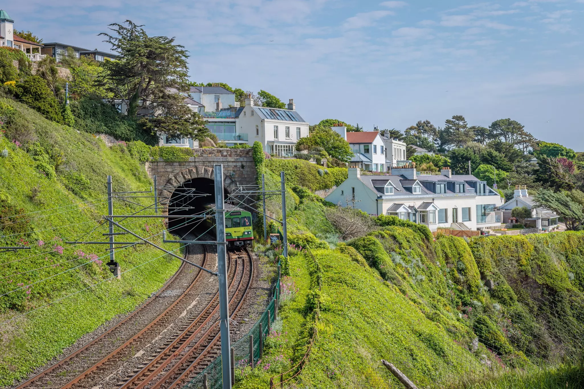 A train passes houses by a tunnel on a green hillside near Dublin, Ireland.