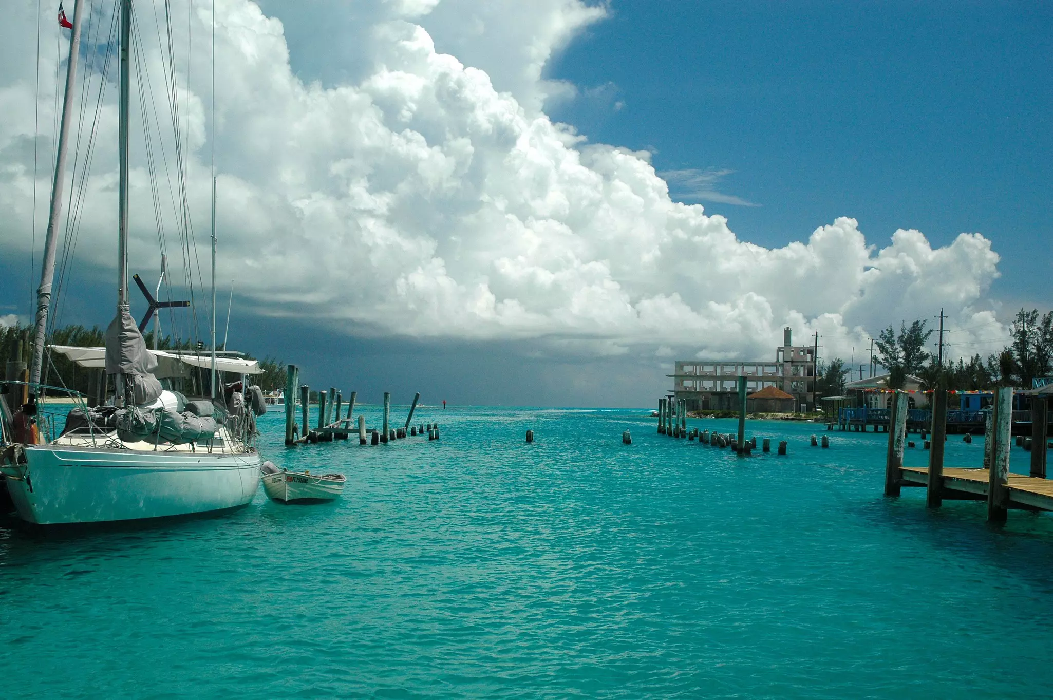 A sailboat docked in a small harbor as large clouds roll in the darkening sky over the horizon.