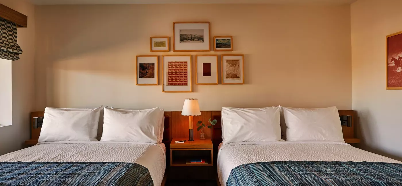 A homey double queen room with framed photographs on the walls.