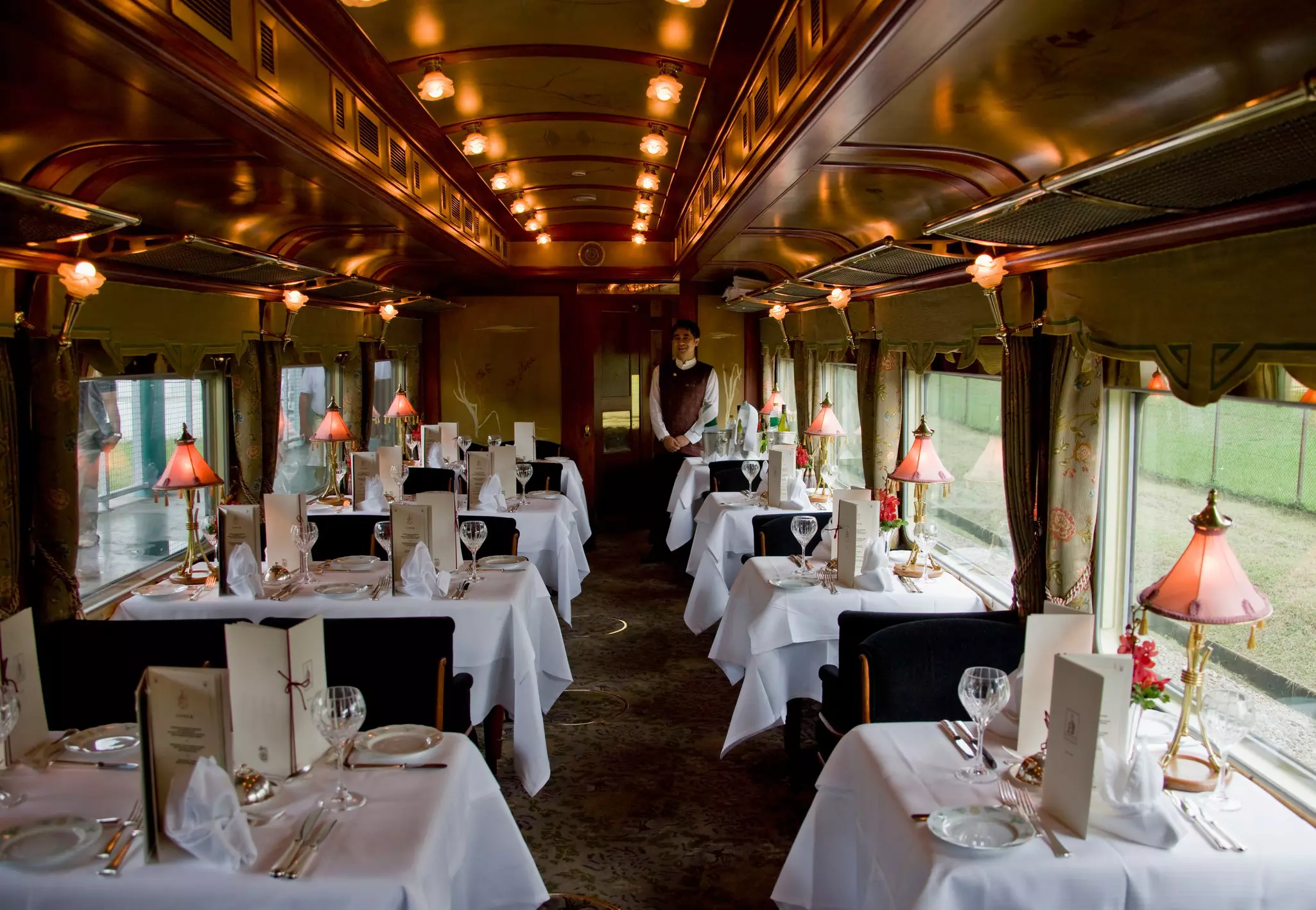 Tables are elegantly set with crystal and white tablecloths in the dining car of a luxury train.