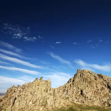 Jagged lichen-covered volcanic rock ridge on a hilltop against a deep blue sky streaked with wispy clouds