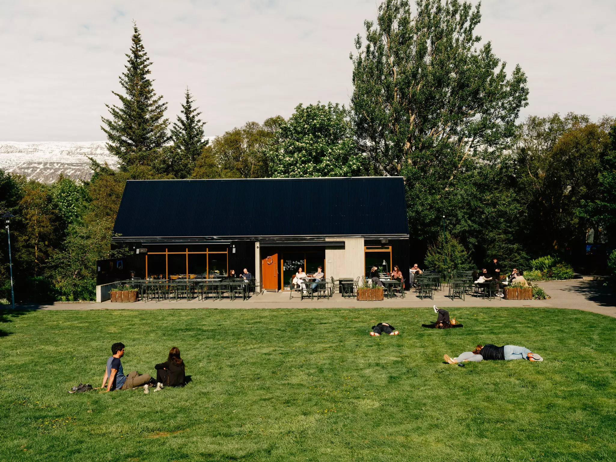 A black roofed building in a botanical garden with people lounging and enjoying the sun outside